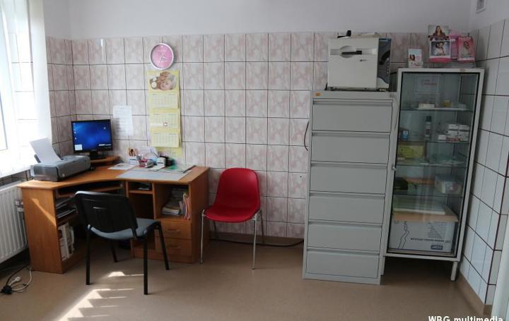 Gabinet lekarski - biurko, szafa z szufladami na dokumenty, obok przeszklona witryna na leki